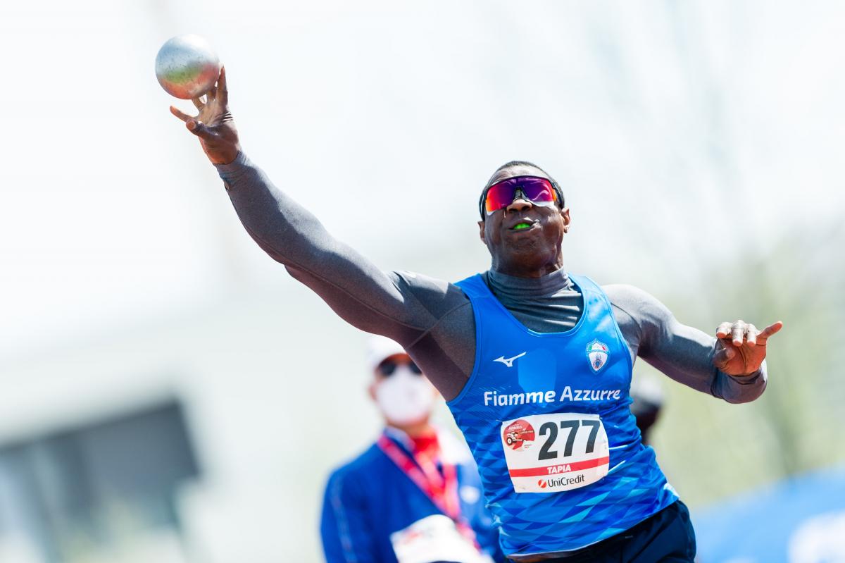 A man competing in shot put observed by another man 