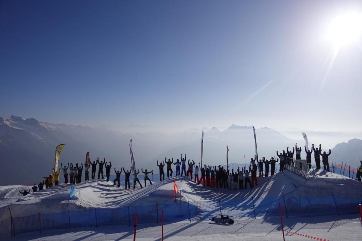 Snowboarders line up along a border-cross slope with their arms raised