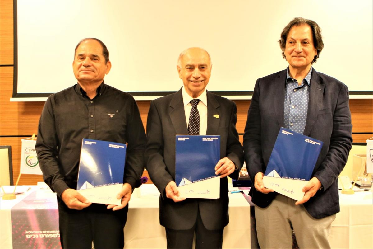 Three men in suits smiling holding a folder