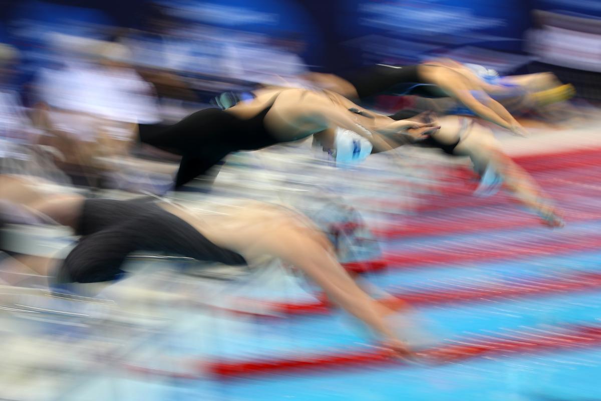 A blurred picture of a group of female swimmers jumping in the pool