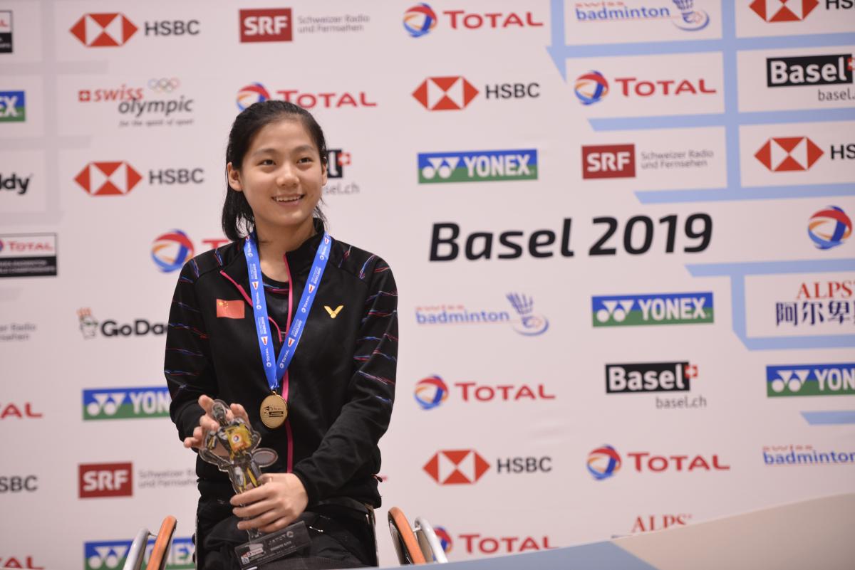 Chinese badminton player Liu Yutong smiles while holding a trophy on the podium