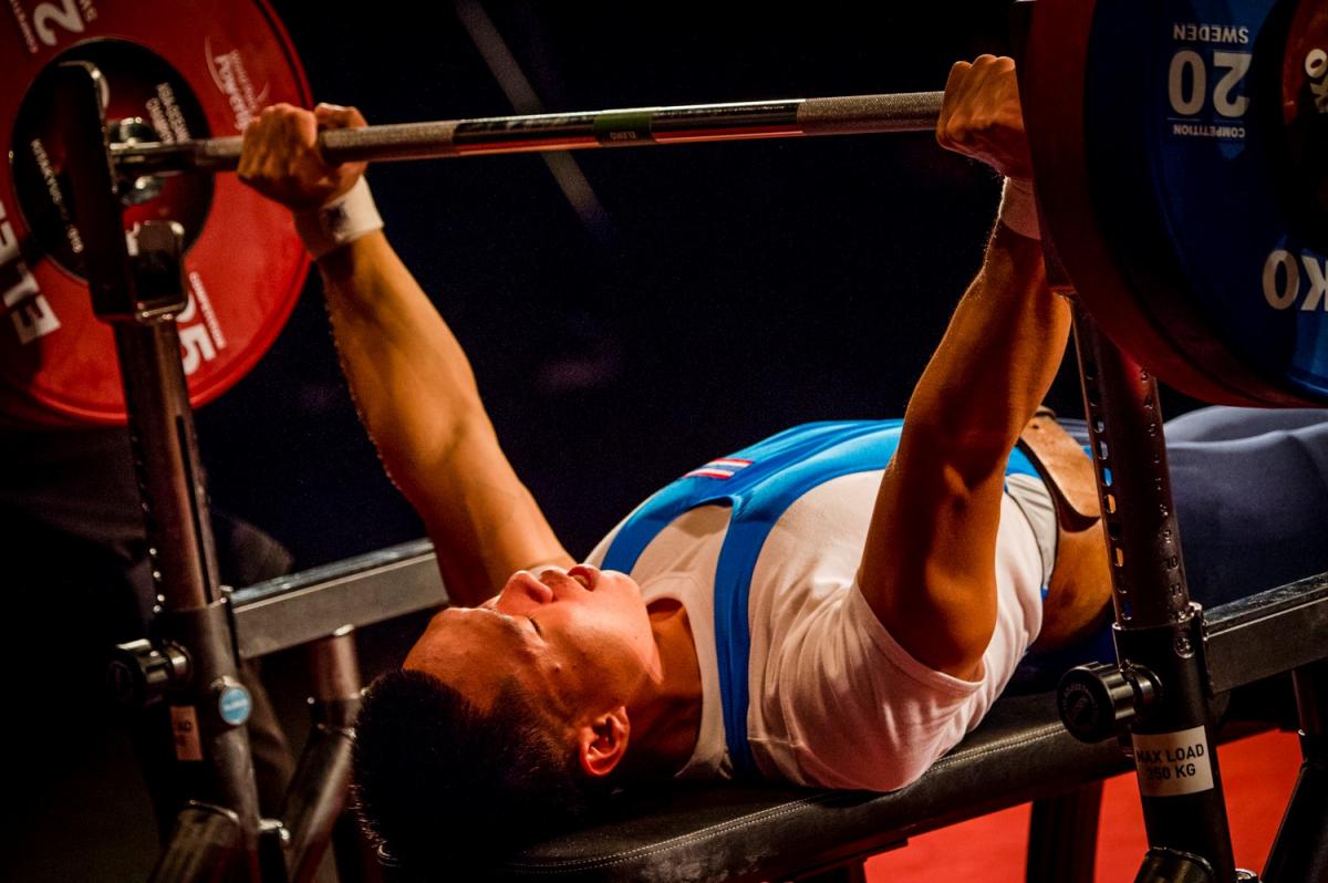 A man on a bench press lifting a bar in a Para powerlifting competition