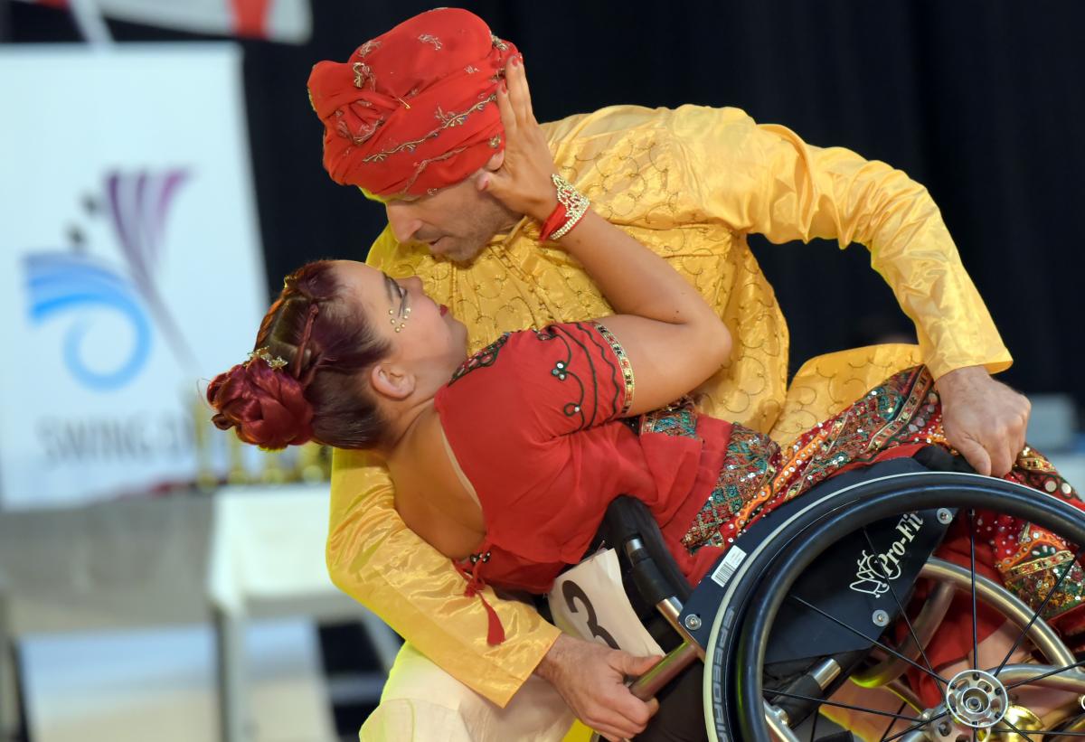 A male standing dancer holding a wheelchair with a female Para dancer during a competition