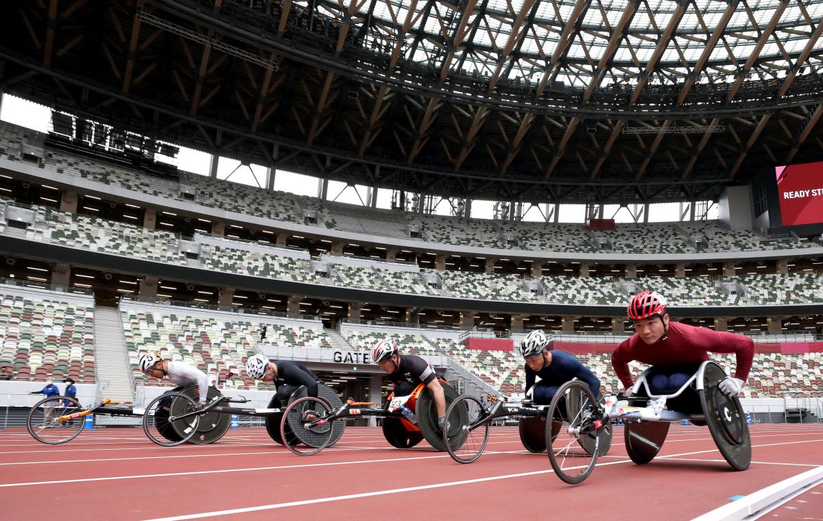 A group of five male wheelchair racers on an athletics track in an empty stadium