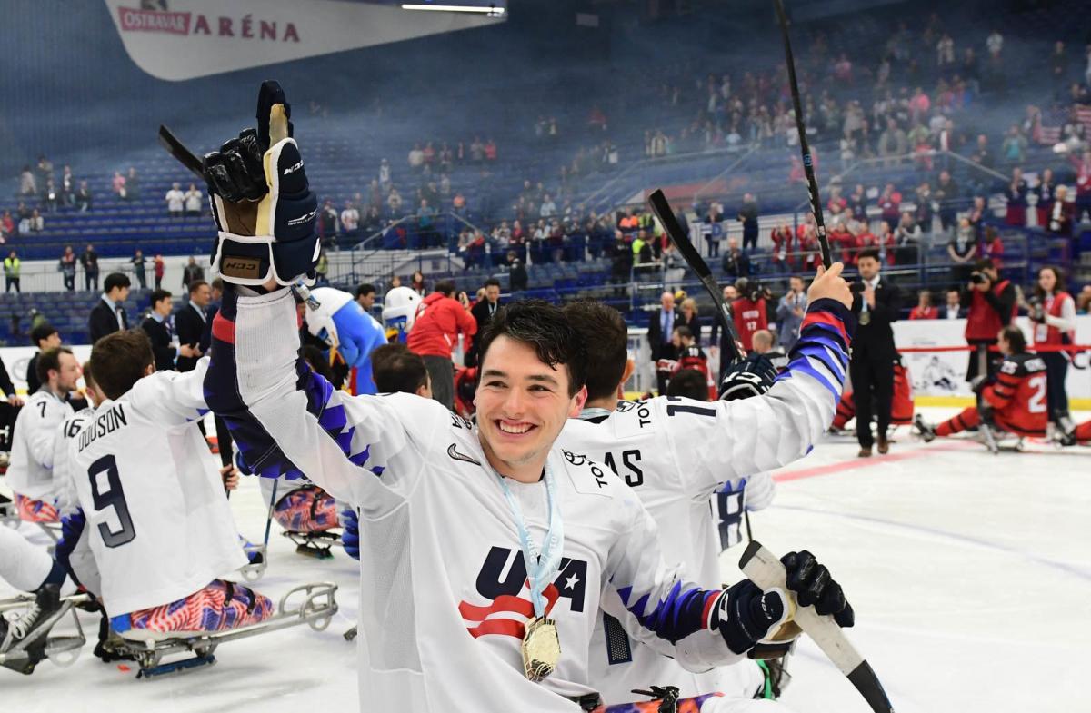 A man celebrating with a group of Para ice hockey players on an ice rink after a match in an indoor arena