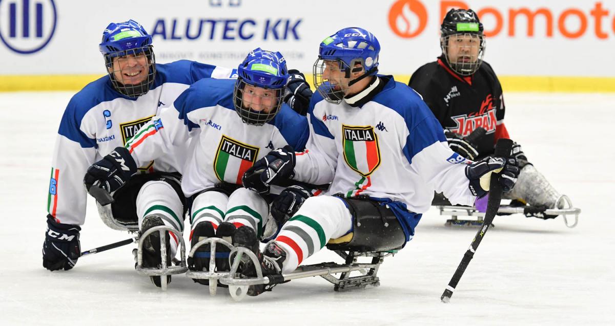 Three Para ice hockey players with the uniform of Italy celebrating with another player from Japan observing