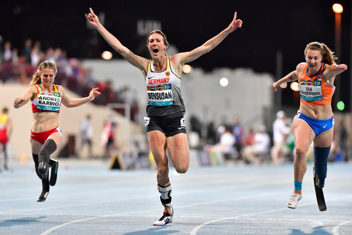 A female athlete celebrating after finishing a race ahead of two other women with prosthetic legs