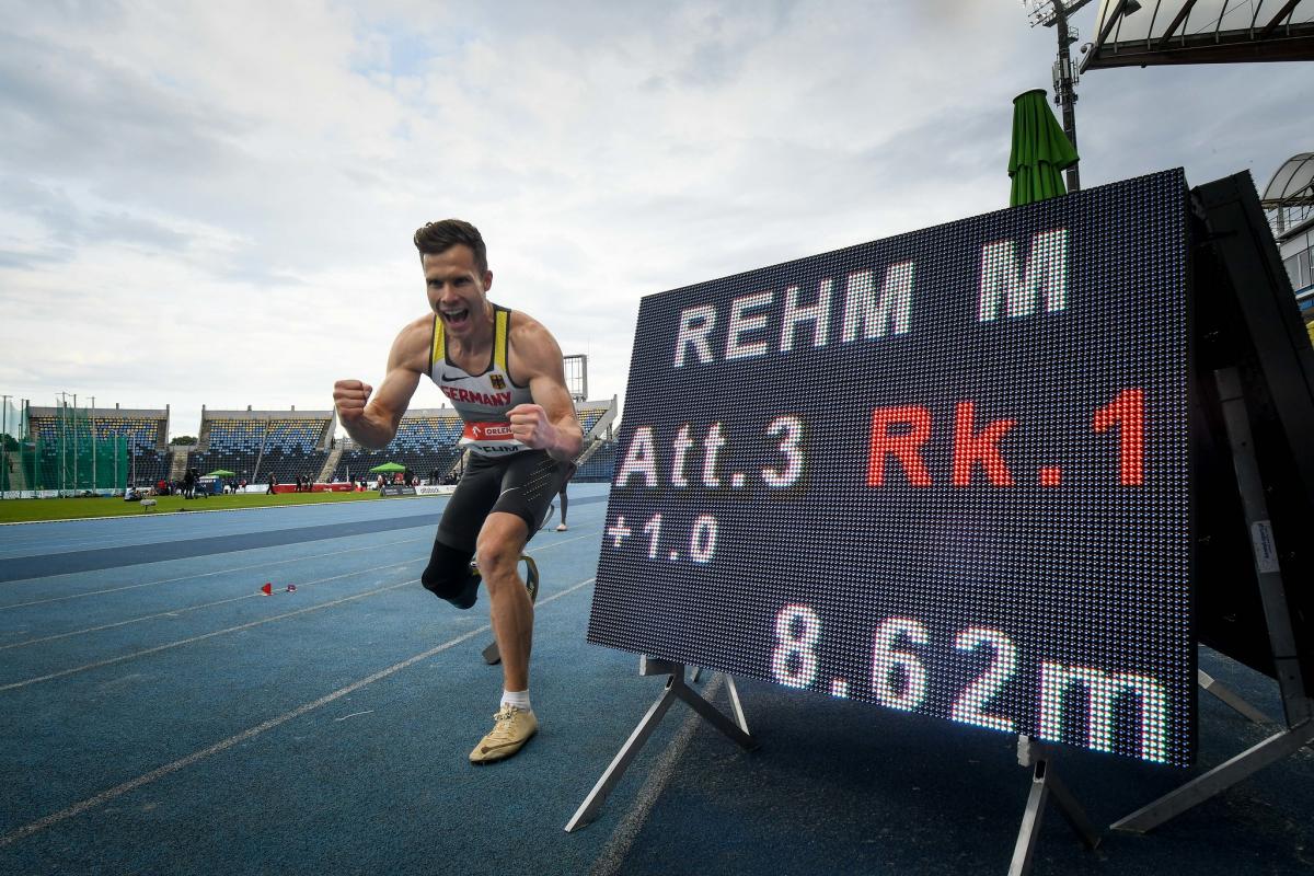 A man with a prosthetic leg celebrating in an athletics track next to a screen showing his world record result