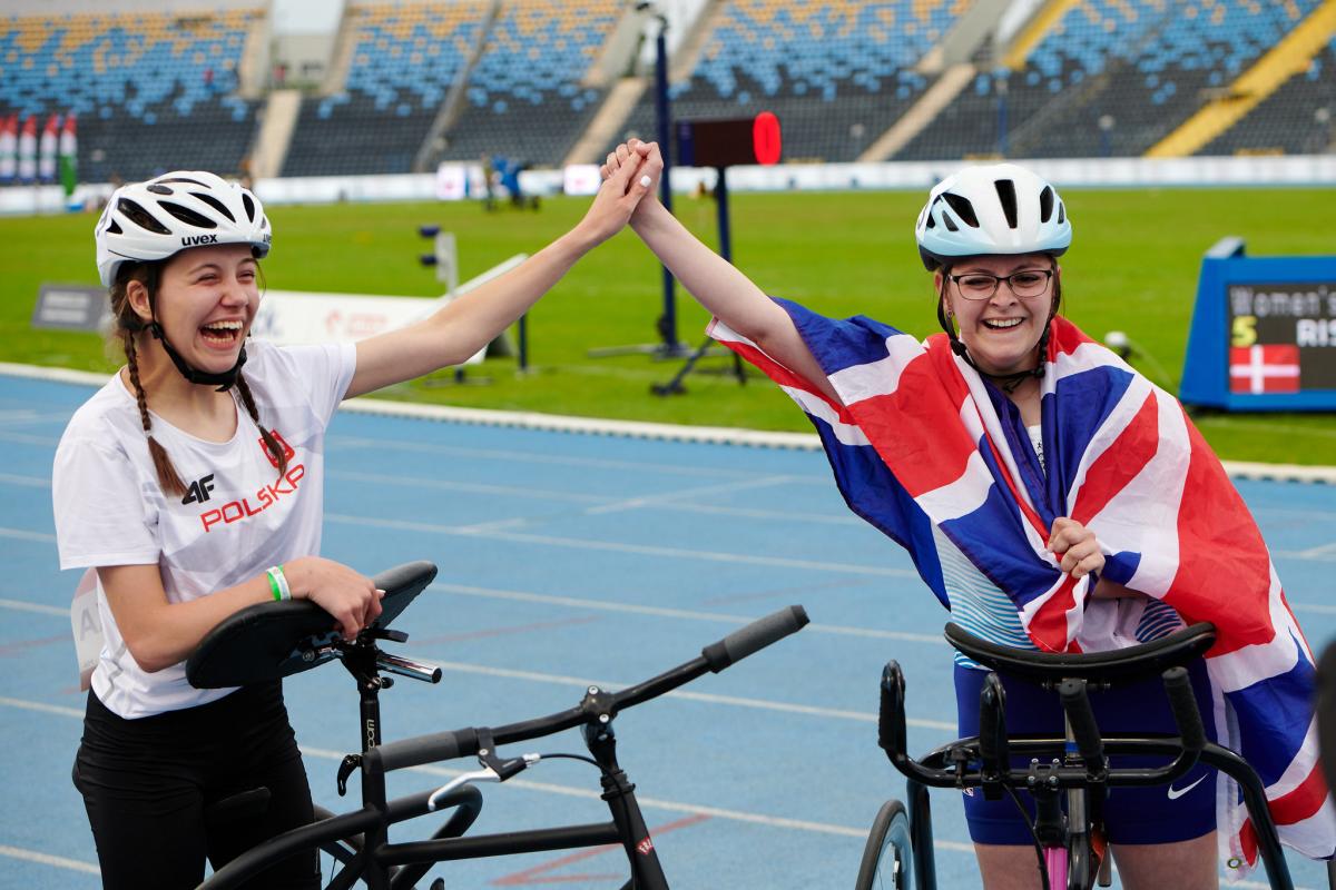 Two young women holding hands on an athletics track