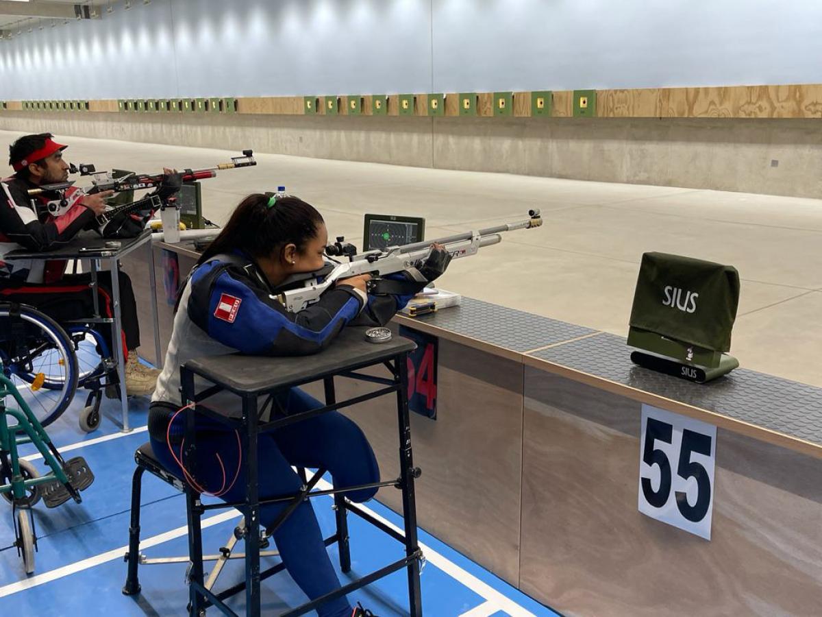 A female leg amputee and a men in a wheelchair practicing shooting in an indoor shooting range