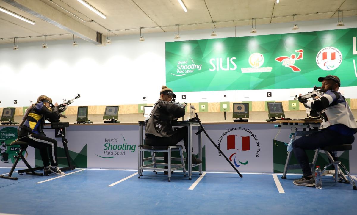 Three persons seated and shooting with rifles in a shooting range