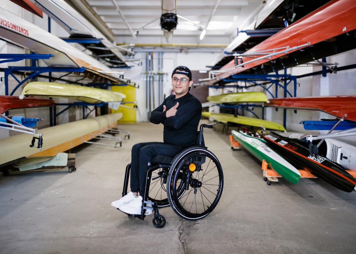 Anas Al Khalifa in his wheelchair posing to the camera while surrounded by kayaks