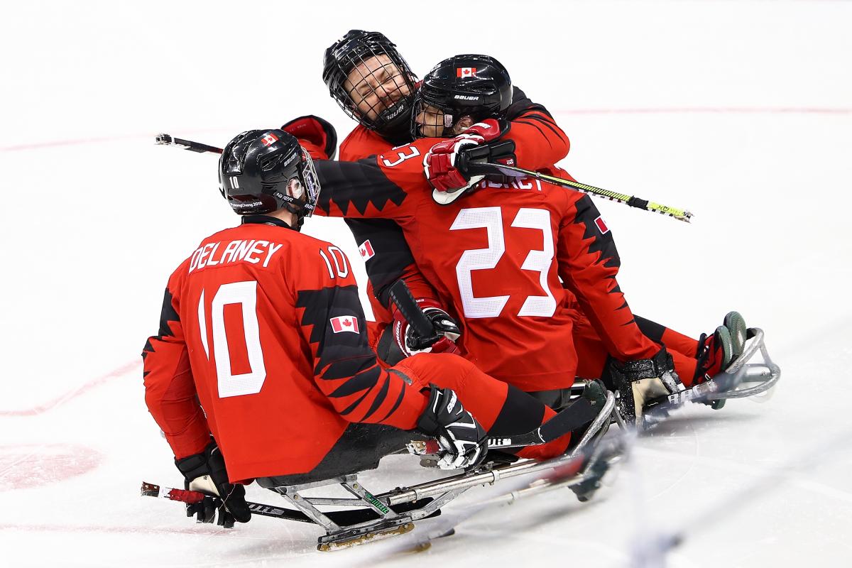 Three Canadian Para ice hockey players hugging in celebration during a game