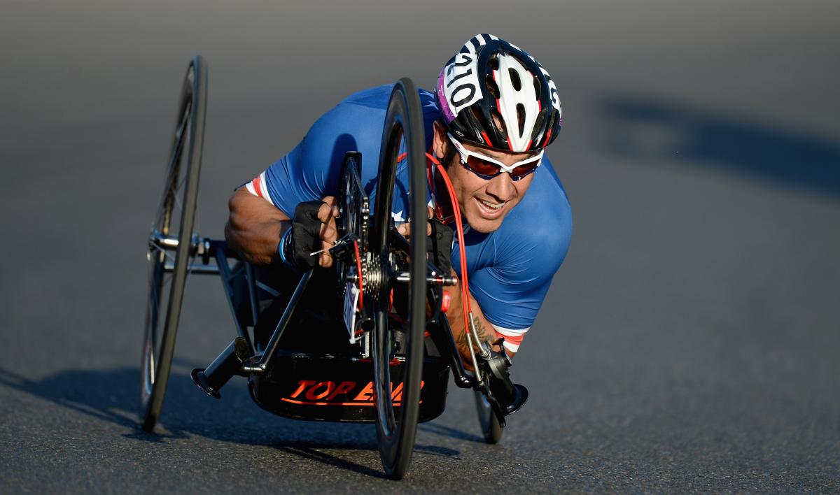 Close shot of US Para cyclist Oz Sanchez as he makes a turn on his handcycle while wearing Team USA gear