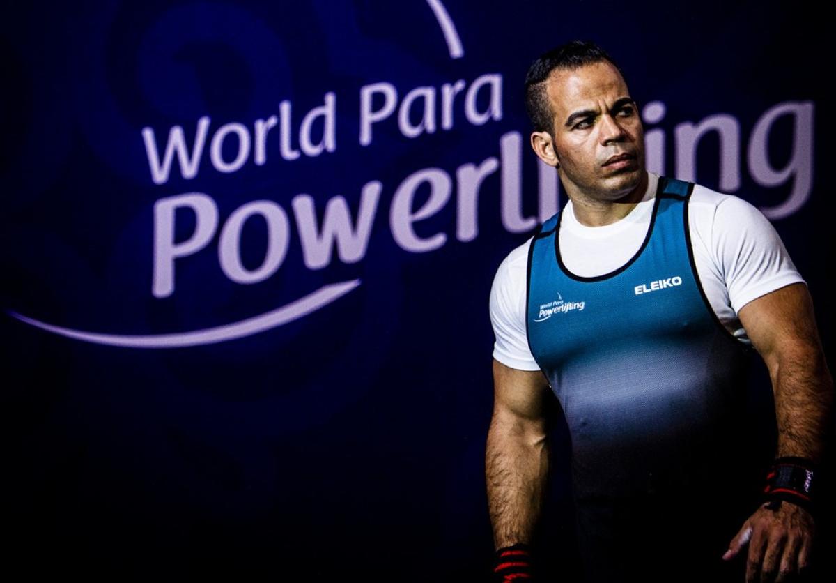A man walking on a stage with a logo of World Para Powerlfiting in the background
