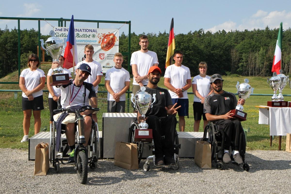 Three men in wheelchairs holding trophies with seven persons standing behind them
