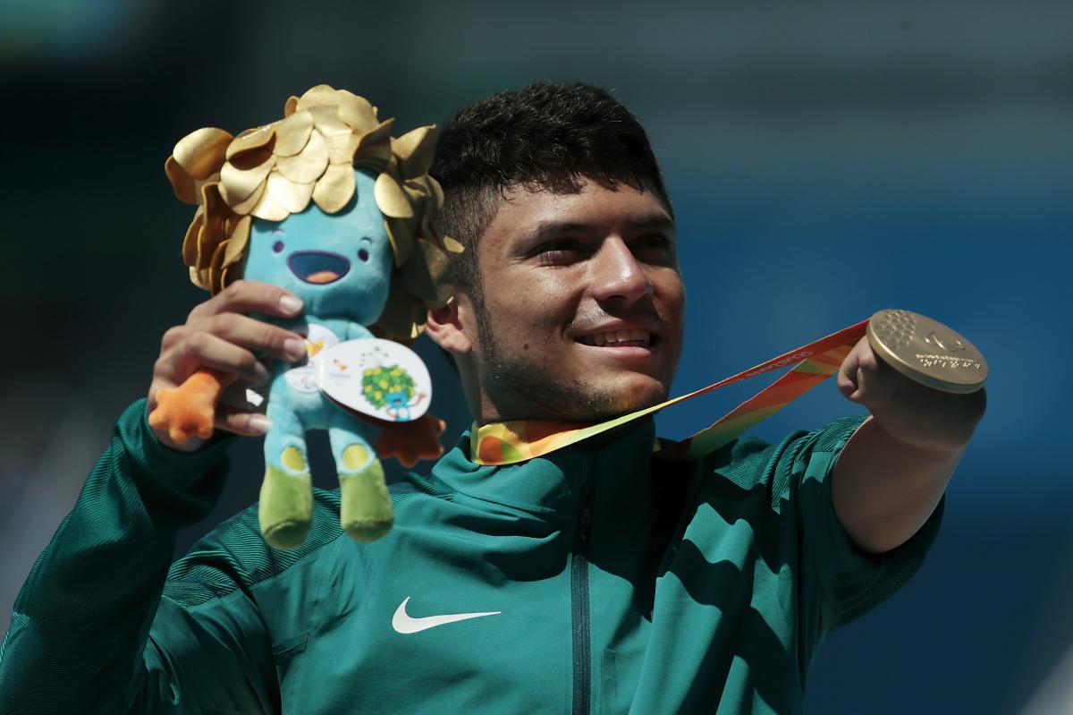 A man without an arm holding a mascot and showing his gold medal