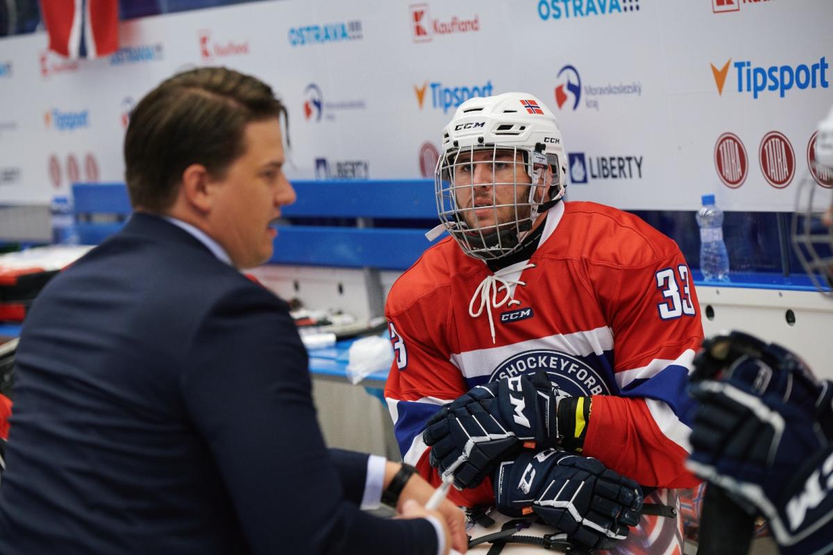 A man in a Para ice hockey uniform talking to another man in a suit in a Para ice hockey game