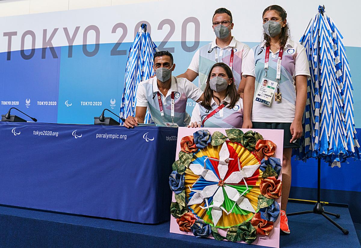 Four athletes of the Refugee Paralympic Team stand in front of a press conference background 