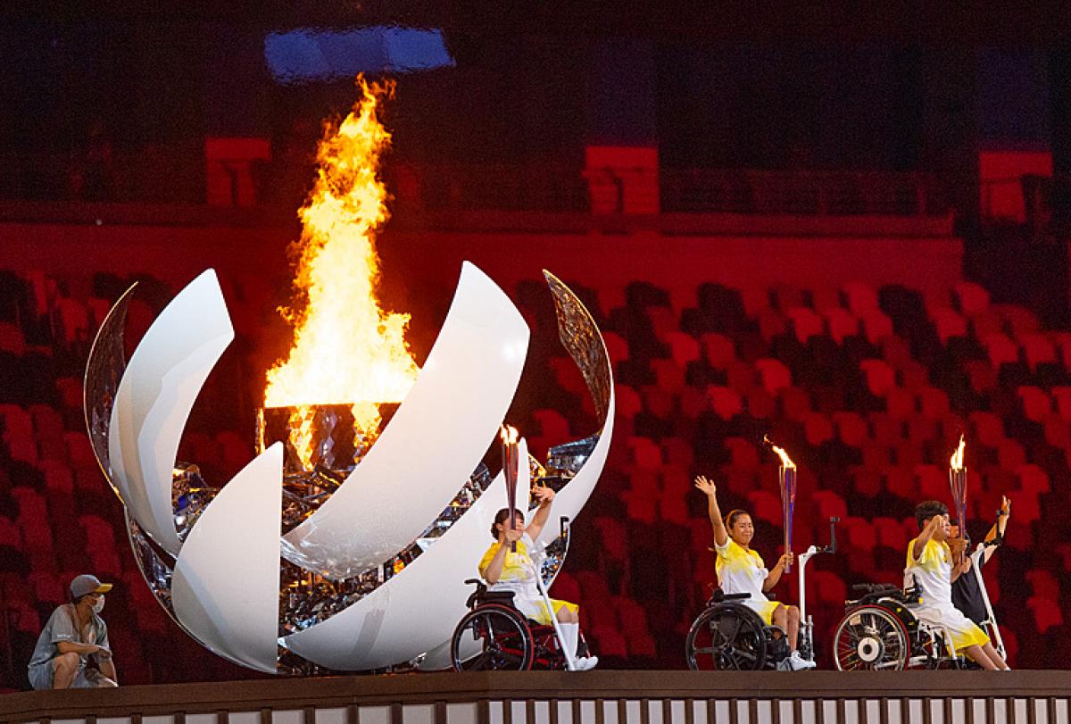 Japanese Para athletes Yui Kamiji, Shunsuke Uchida and Karin Morisaki turn and wave after lighting the Tokyo 2020 Paralympic Flame