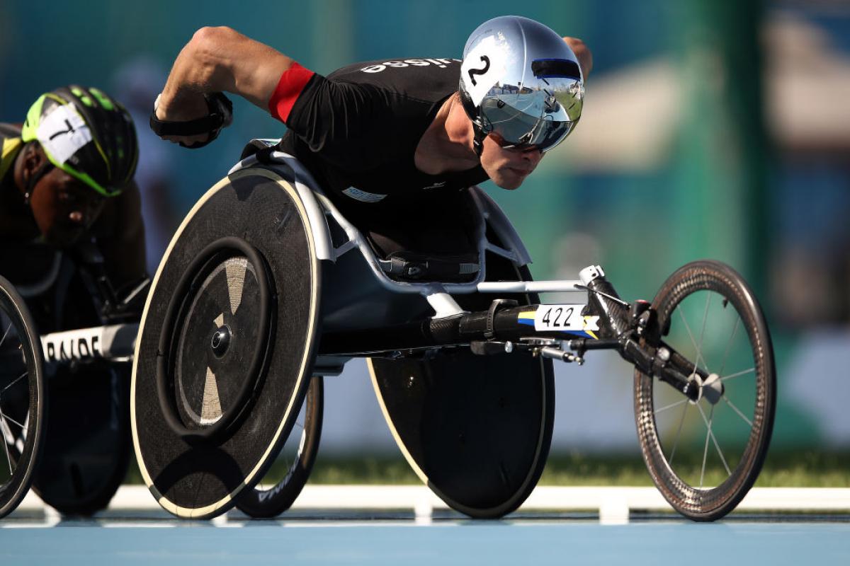 A man with a helmet pushes his wheelchair with pneumatic tyres in the Para athletics track event