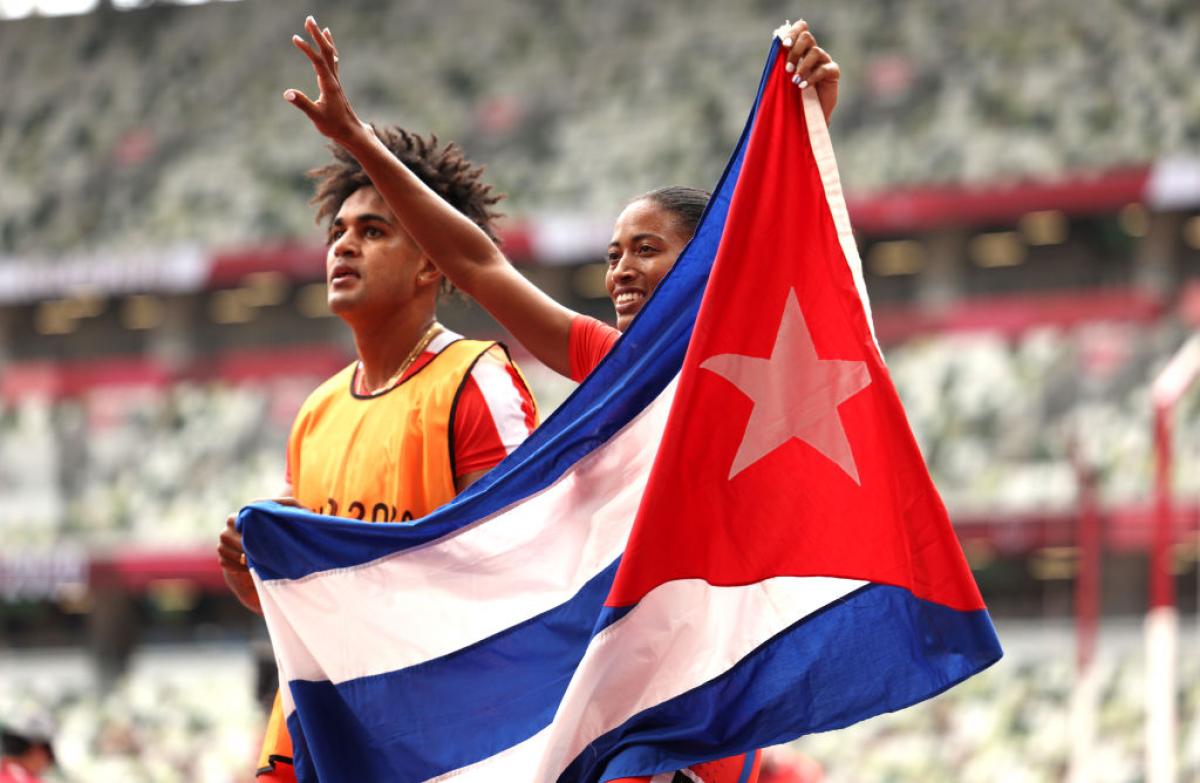 A male and a female sprinter holding the flag of Cuba in an athletics stadium