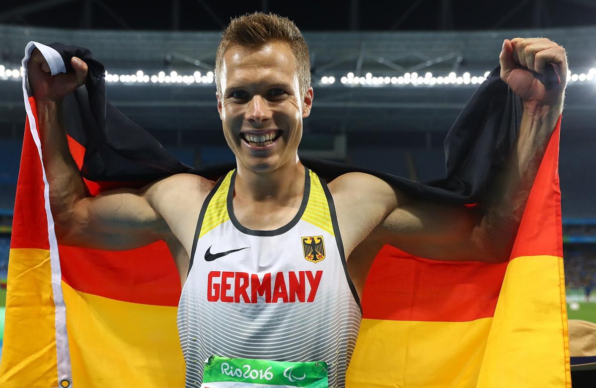 An smiley athlete holding the German flag behind his back