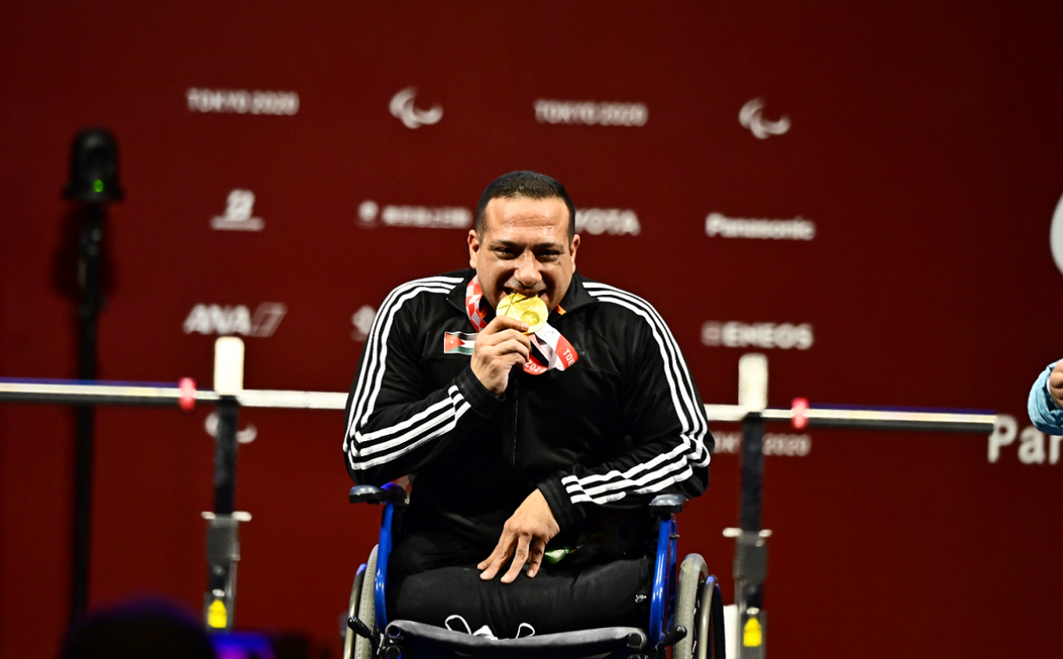 A man in a wheelchair biting his gold medal