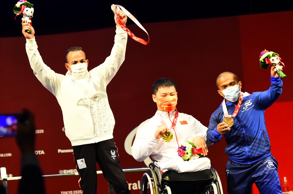 Three men showing their medals on a stage