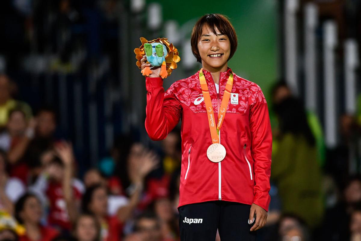 Japanese female judoka smiles on podium holding Paralympic mascot gift