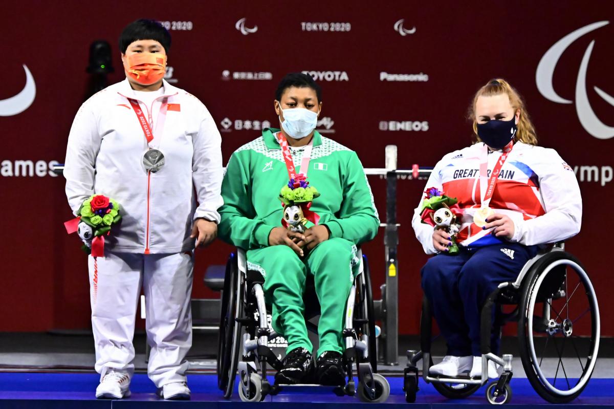 Three women posing for photos on the podium with their medals