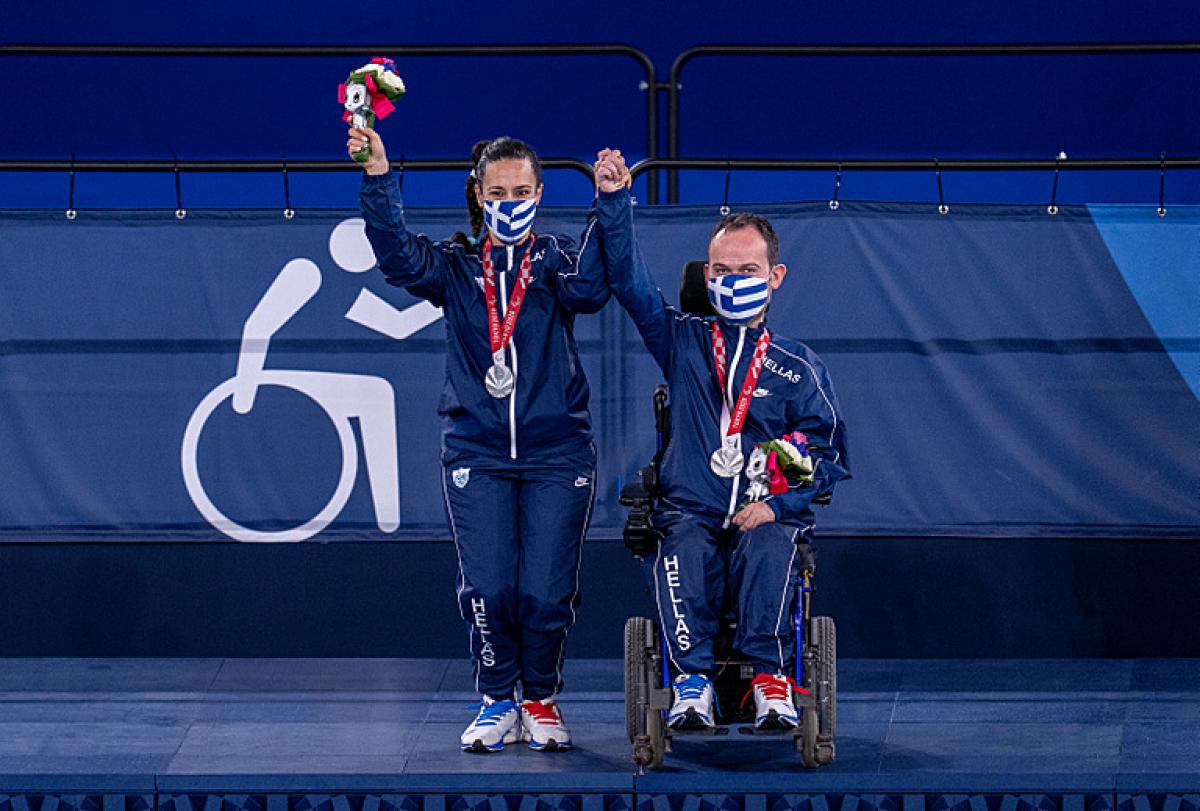 Grigorios Polychronidis with his wife and assistant hold up their hands to celebrate their silver medals