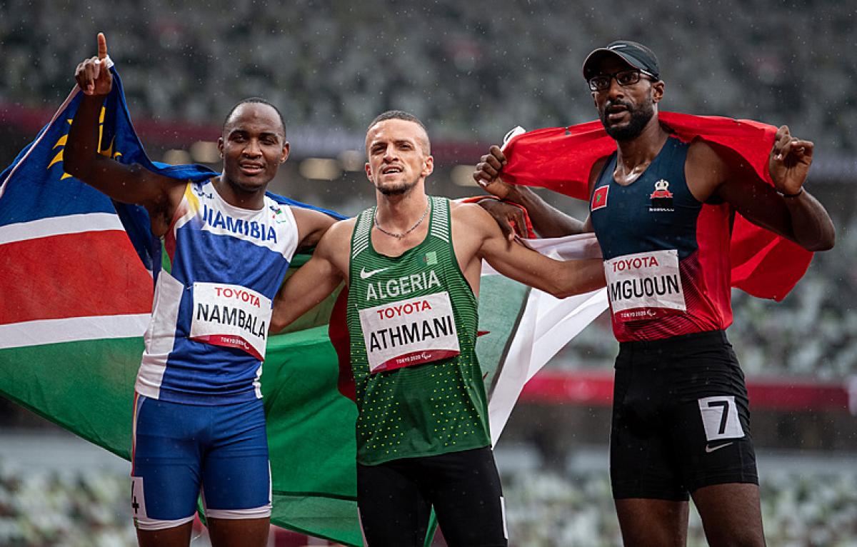 Three men on an athletics track with their flags 