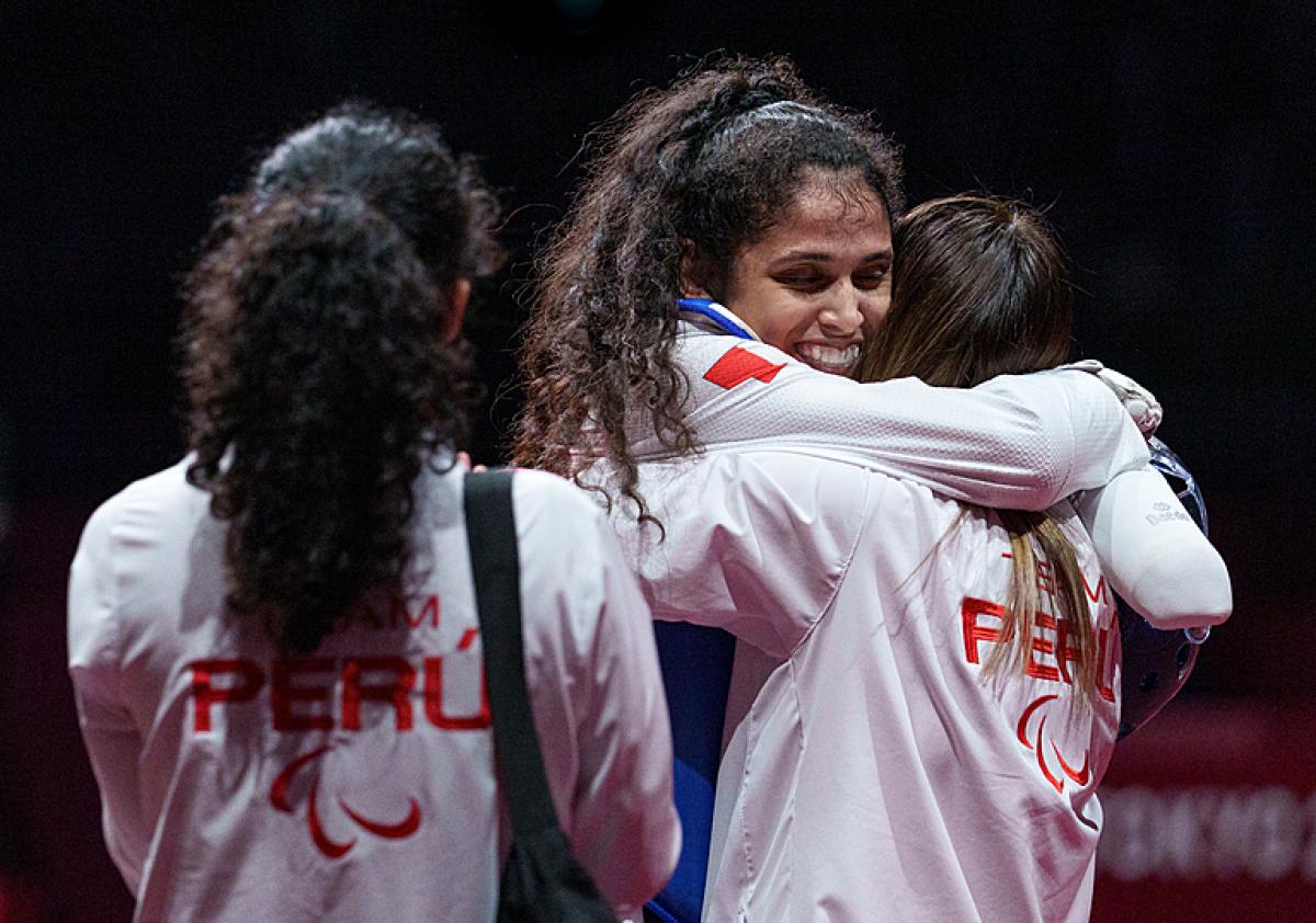 Leonor Espinoza Carranza smiles and hugs a colleague wearing a white jacker with peru on the back