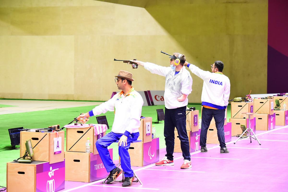 Three male pistol shooters competing in a shooting range