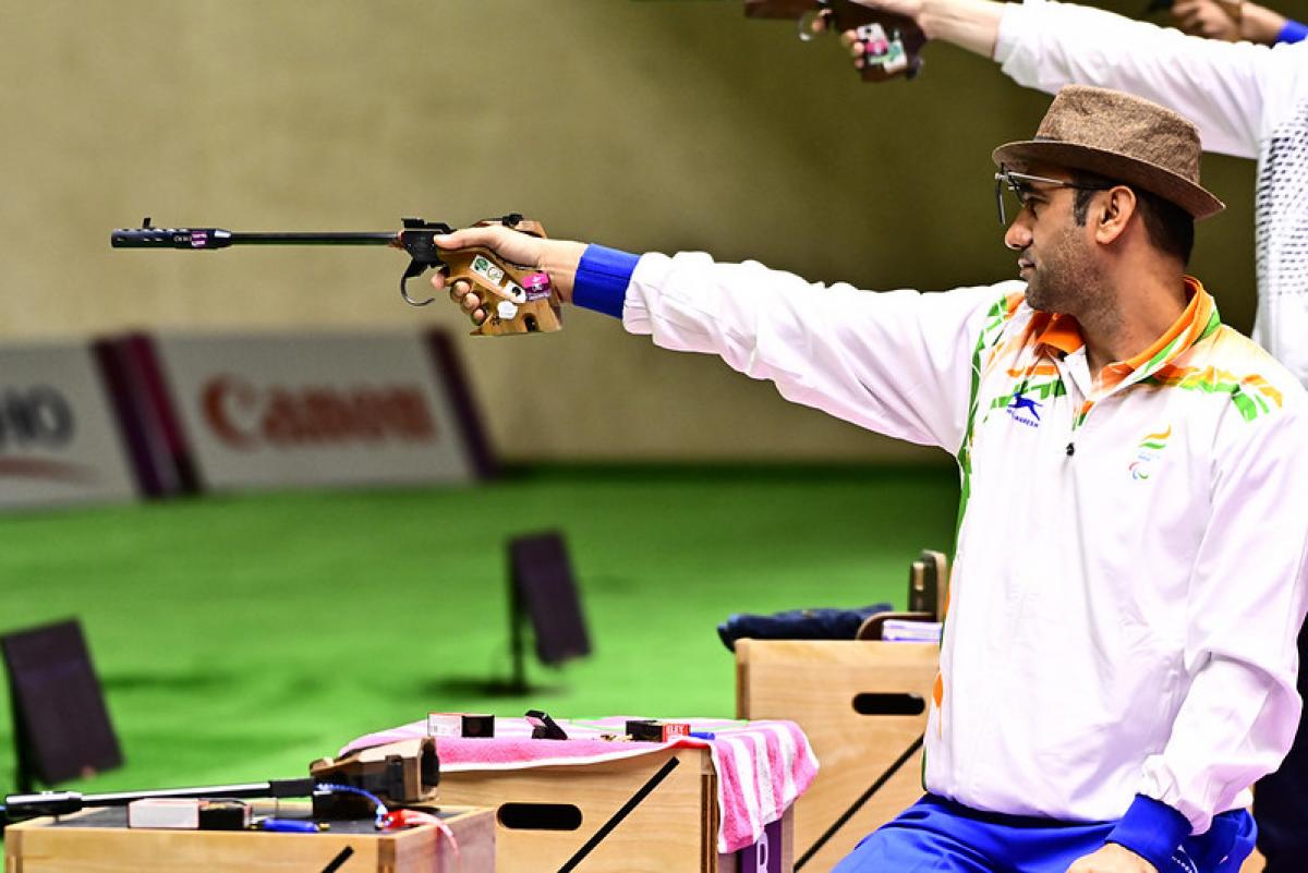 A man with a hat competing in a pistol shooting event in a shooting range