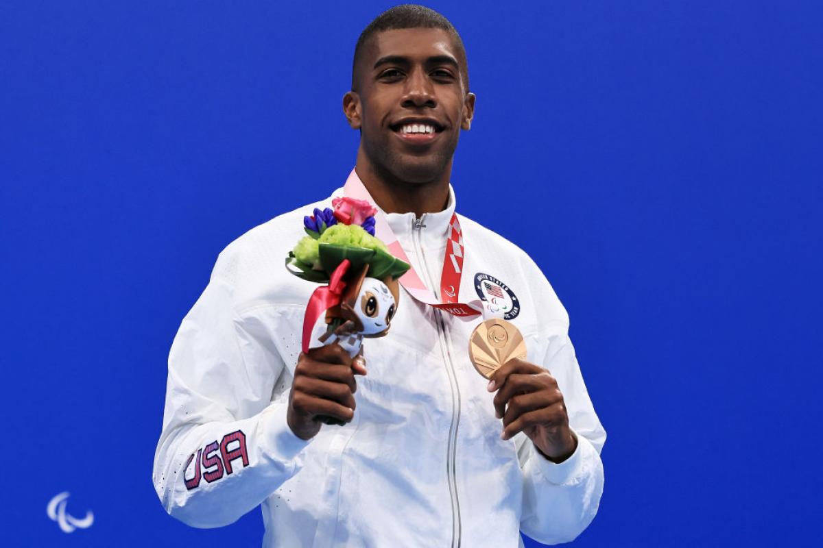 A man with the uniform of USA on a podium holding his medal 