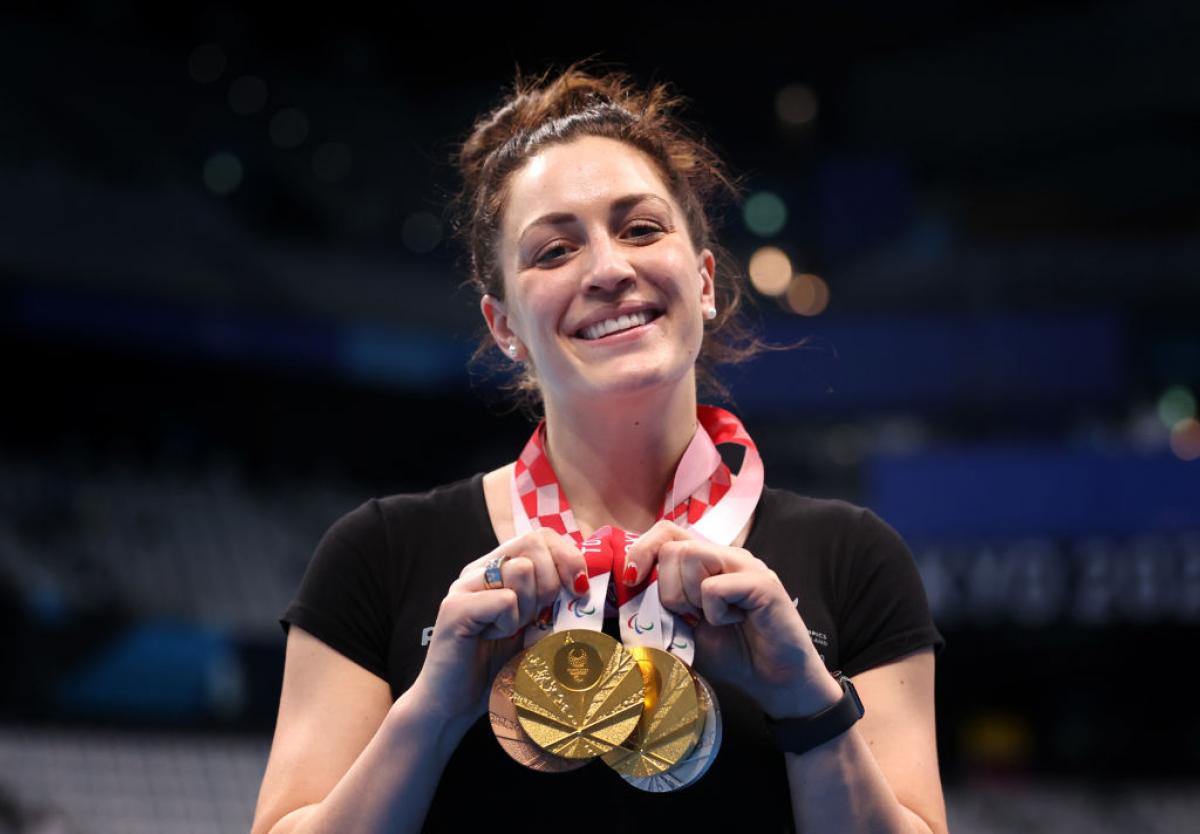 A Para swimmer posing with four medals and smiling to the camera