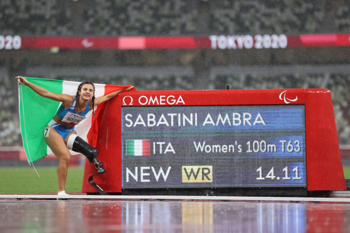 A woman with a prosthetic leg standing next to a screen showing her name and record on an athletics track