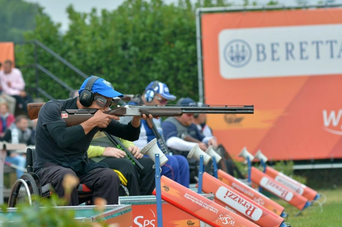A man in a wheelchair competing with a shotgun in a Para trap event observed by other four competitors