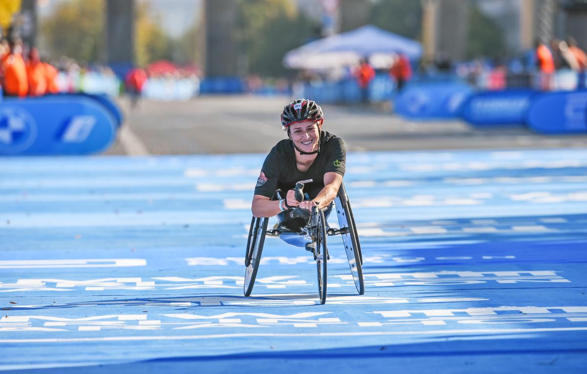 A female wheelchair racer smiling crossing the finish line on a street race
