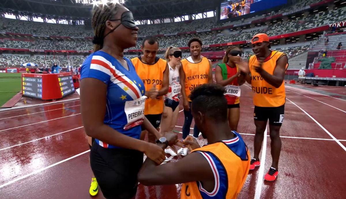 A man kneeling on an athletics track to propose a female athlete surrounded by four people