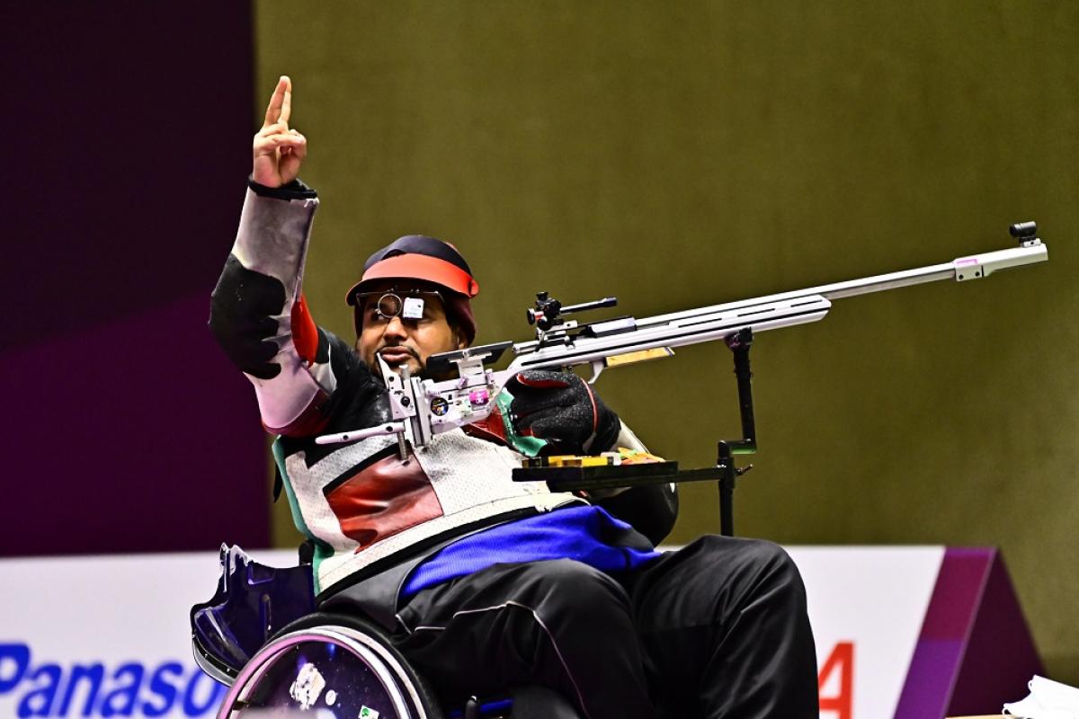 A man in a wheelchair waving in a shooting competition with a rifle