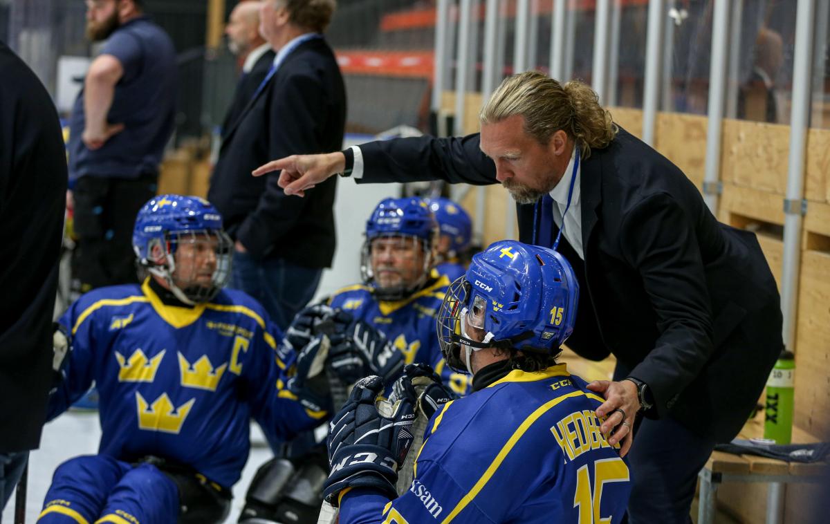 A man talking to Para ice hockey players on sleds pointing finger to the ice