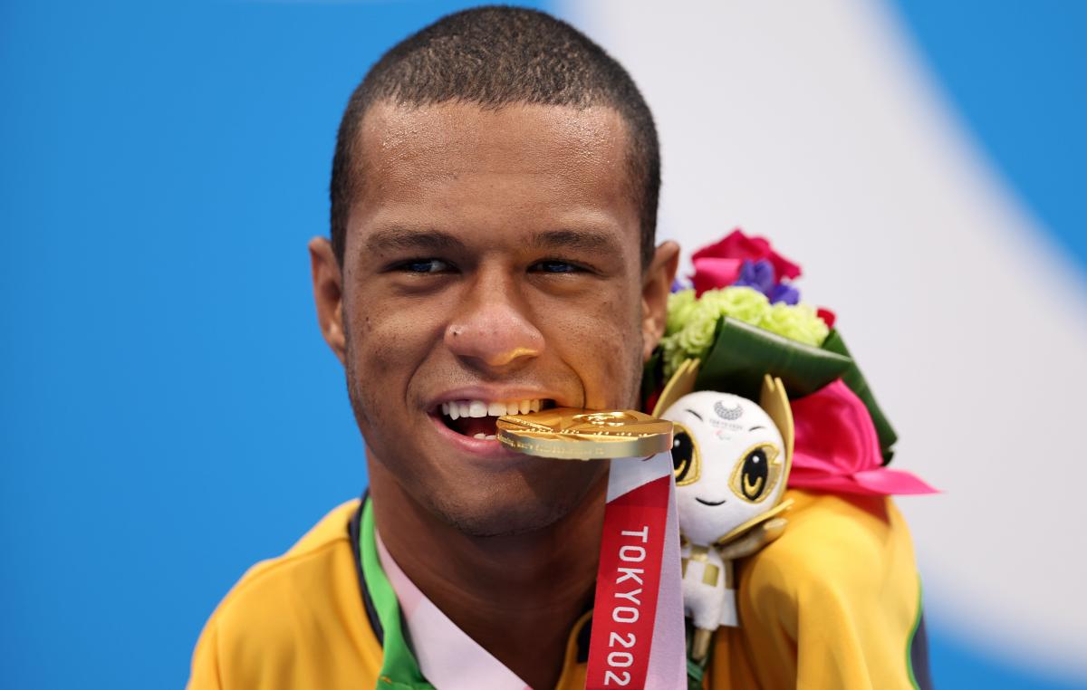 A man poses for photos biting a gold medal