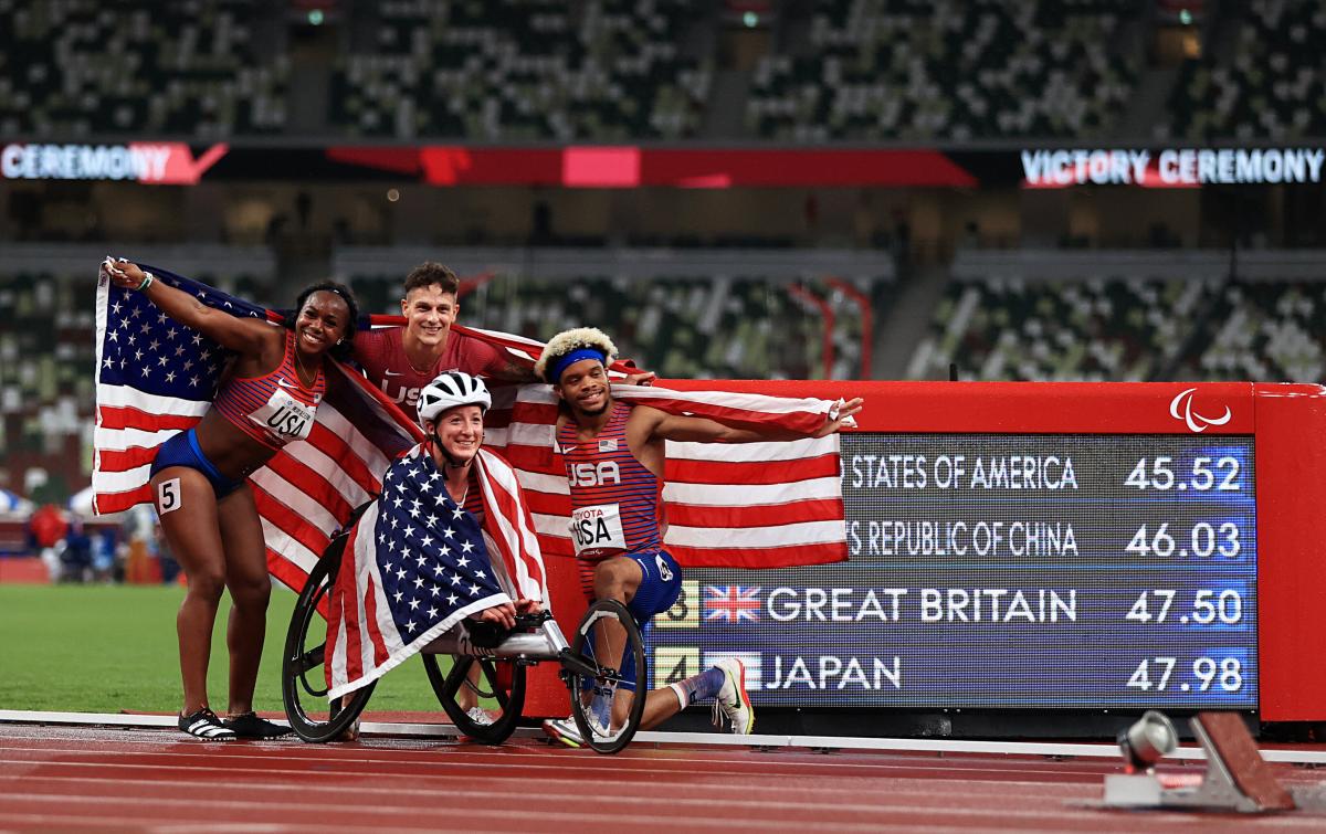 Four athletes celebrating with flags in front ofthe results screen