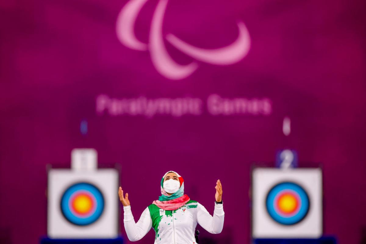 Iranian woman with mask puts hands in air and looks to sky