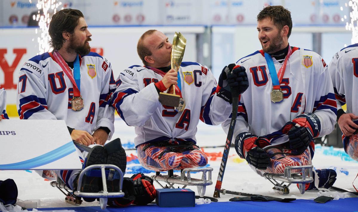 A Para ice hockey player kissing a trophy with the fireworks behind him
