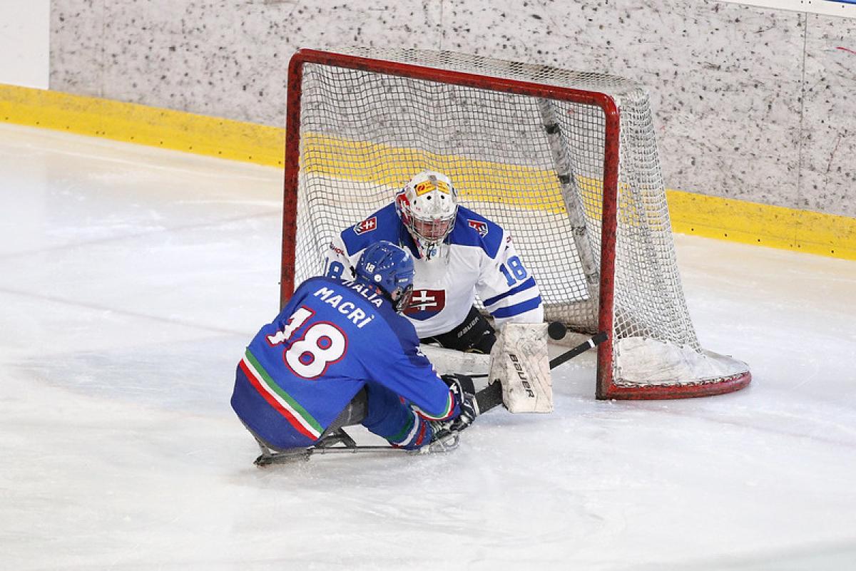 A Para ice hockey player hitting the puck in front of the goaltender