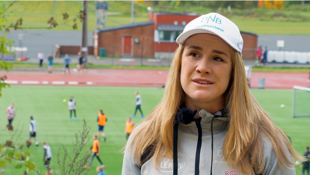 A woman with a white cap talking with a football match in the background